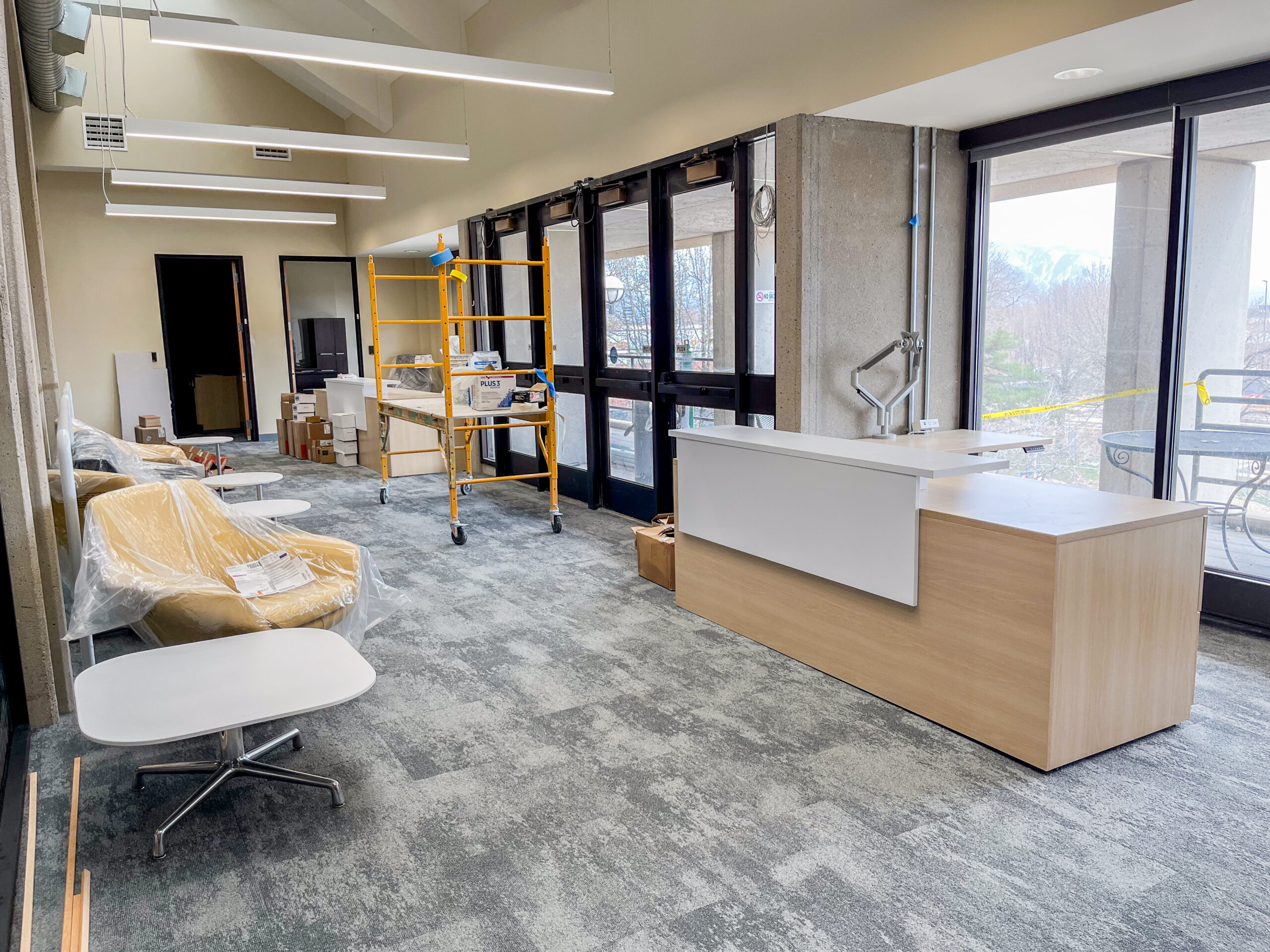 Open lobby area under construction with scaffolding and office furniture covered in plastic.